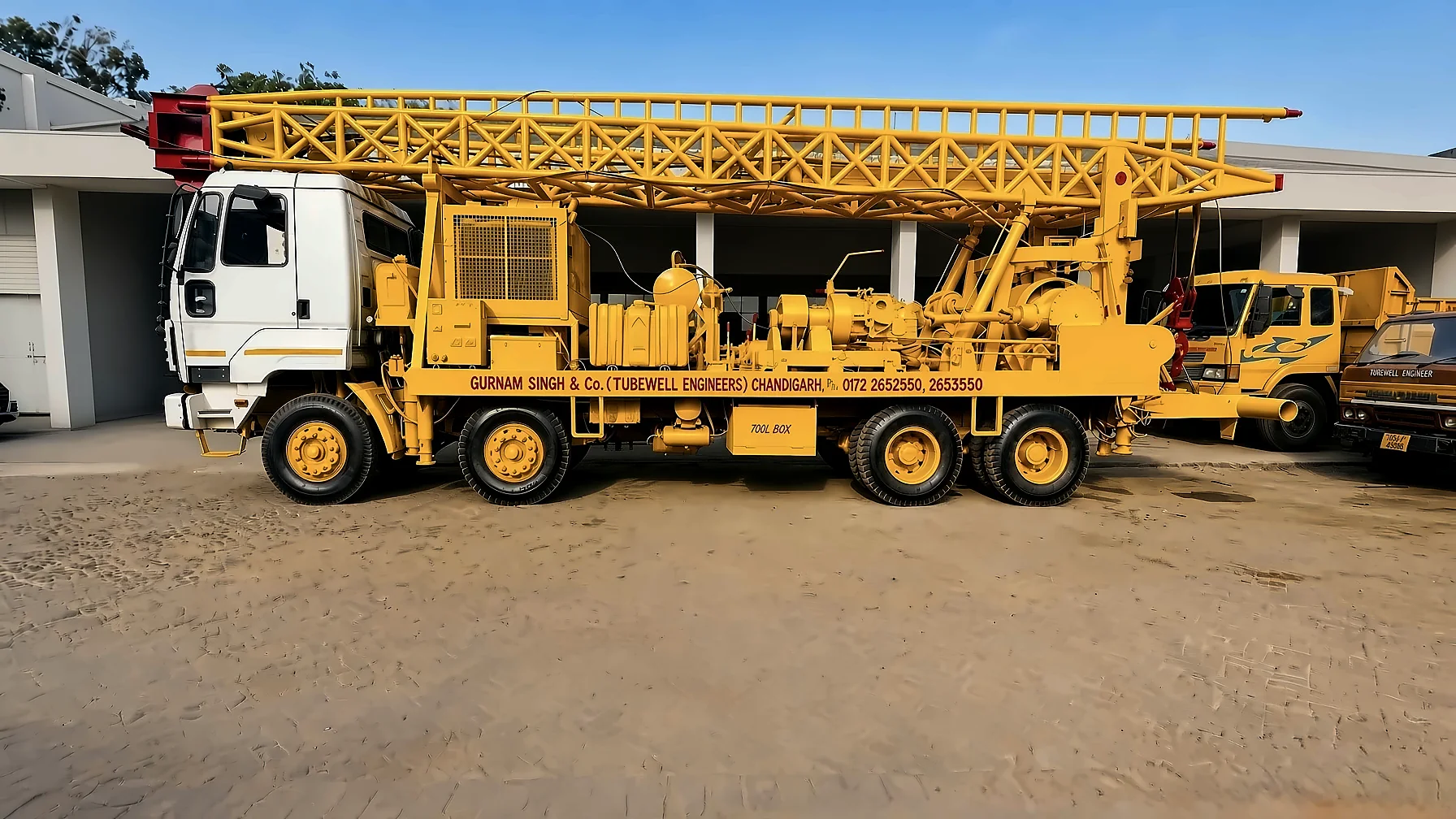 Long lattice-mast drilling rig racked for transit over a white cab at the Chandigarh yard